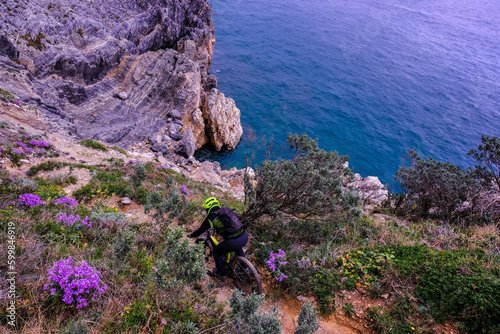 Unrecognisable mountain biker descends on a challenging trail steep towards the sea, Finale Ligure, Italy