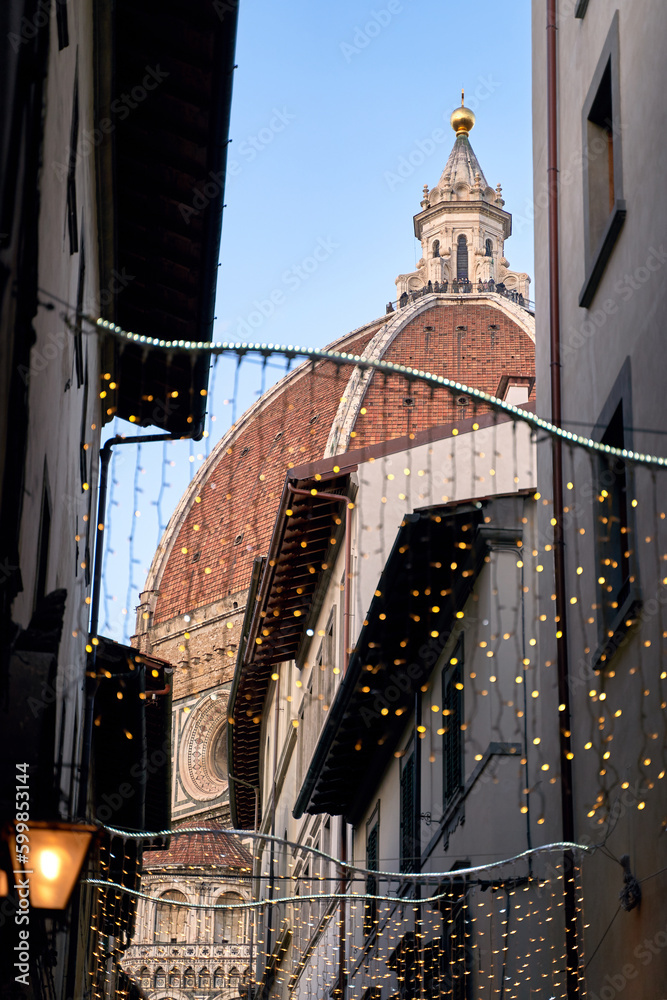 View of the Cupola of the Dome of Florence Cathedral or Duomo from the narrow city street with festive lights