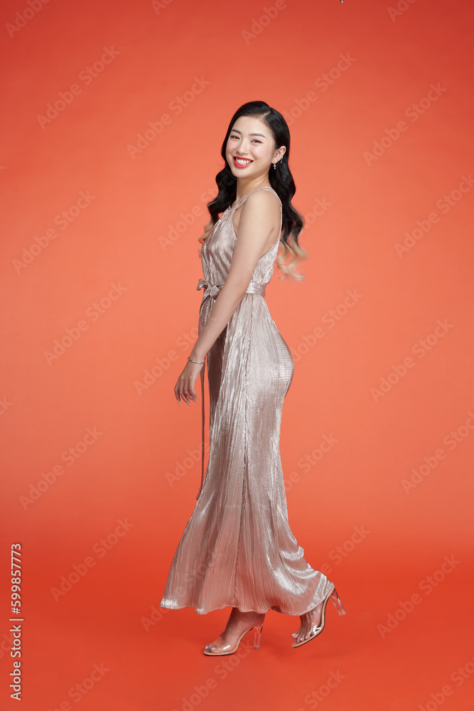 Elegant lady in silver sequins shiny dress standing and posing against red background Elegant lady in silver sequins shiny dress standing and posing against red background