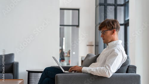 Businessman side view typing in laptop sitting on sofa in modern apartment