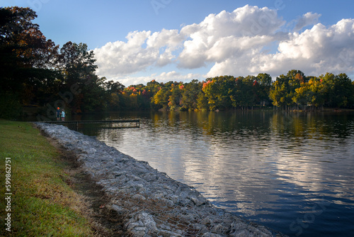Boy and girl on a dock fishing on a lake with clouds and fall colored trees in the background.