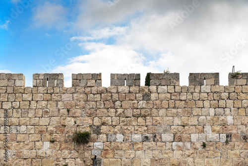 Background with fragment of the upper part of the fortress wall of Jerusalem Old City with the blue sky and clouds on the background