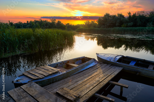 Evening landscape with an old rustic wooden pier and old boats at sunset on the Dnieper Delta