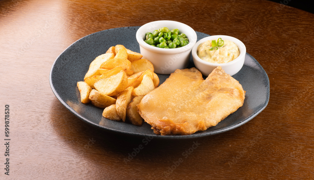 plate of fish and chips with sliced ​​fried fish and pub table close-up with tartar sauce and green peas