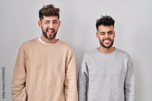 Young homosexual couple standing over white background winking looking at the camera with sexy expression, cheerful and happy face.