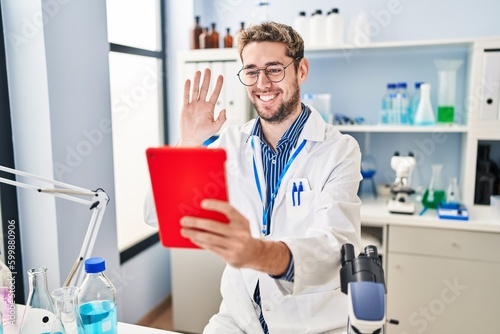 Hispanic man with beard working at scientist laboratory doing video call looking positive and happy standing and smiling with a confident smile showing teeth