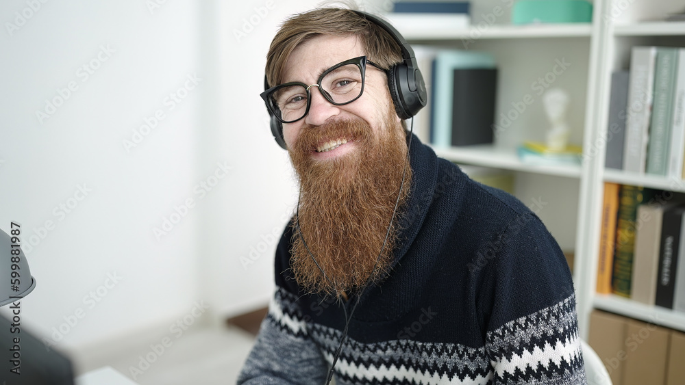 Naklejka premium Young redhead man student using computer and headphones studying at library university