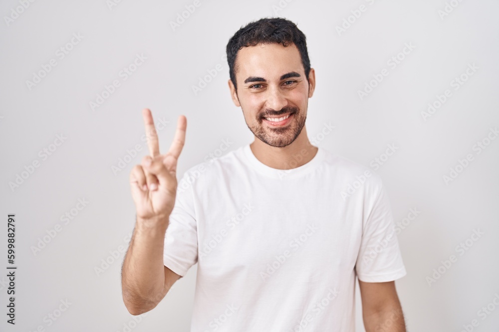 Handsome hispanic man standing over white background showing and pointing up with fingers number two while smiling confident and happy. Handsome hispanic man standing over white background showing and pointing up with fingers number two while smiling confident and happy.