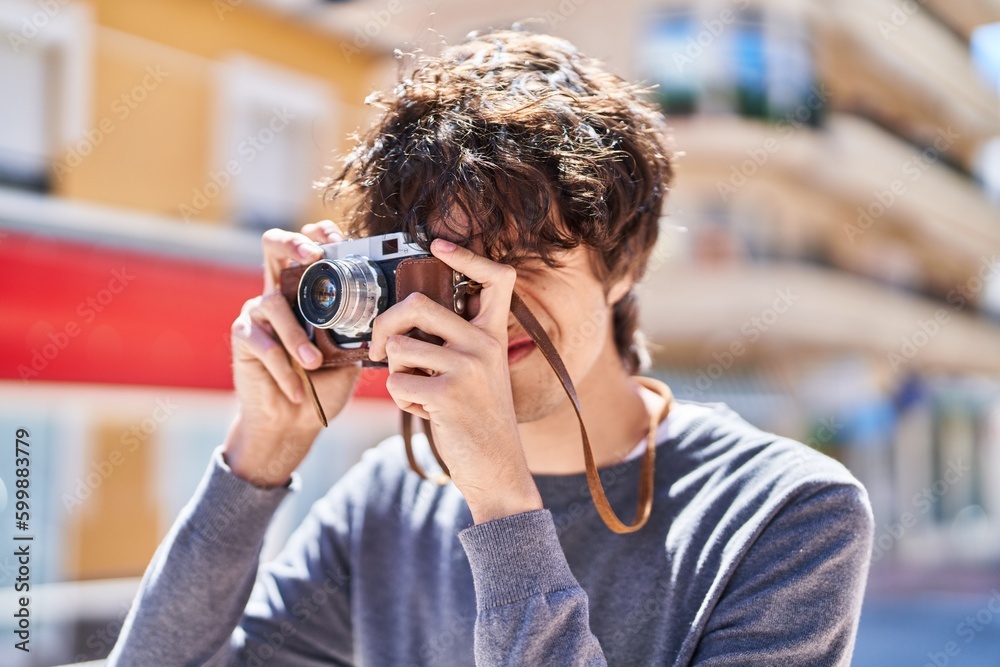 Young hispanic man smiling confident using vintage camera at street