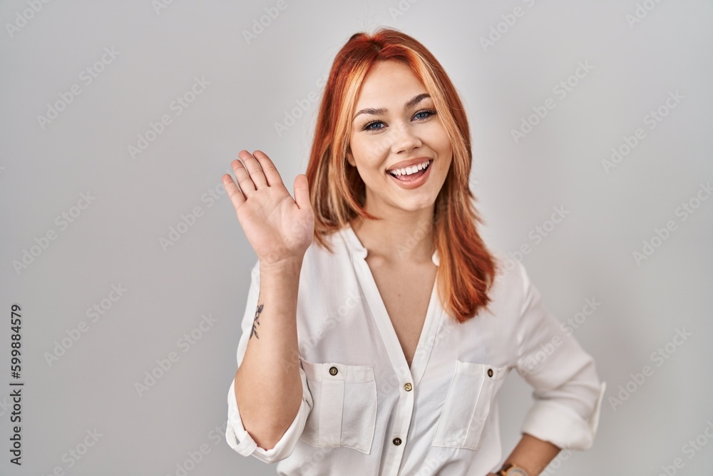 Young caucasian woman standing over isolated background waiving saying hello happy and smiling, friendly welcome gesture Young caucasian woman standing over isolated background waiving saying hello happy and smiling, friendly welcome gesture