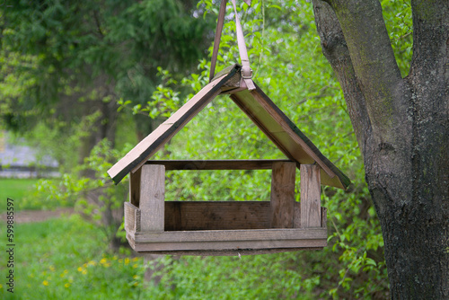 A birdhouse shaped like a cozy little house hangs on a tree, providing a welcoming shelter for birds in the park during spring .