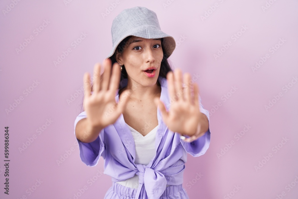 Young hispanic woman standing over pink background wearing hat doing stop gesture with hands palms, angry and frustration expression Young hispanic woman standing over pink background wearing hat doing stop gesture with hands palms, angry and frustration expression