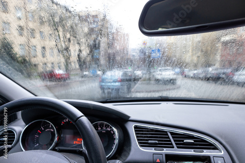 Dashboard of a car interior with a view of a rain-drenched windshield in early spring weather.