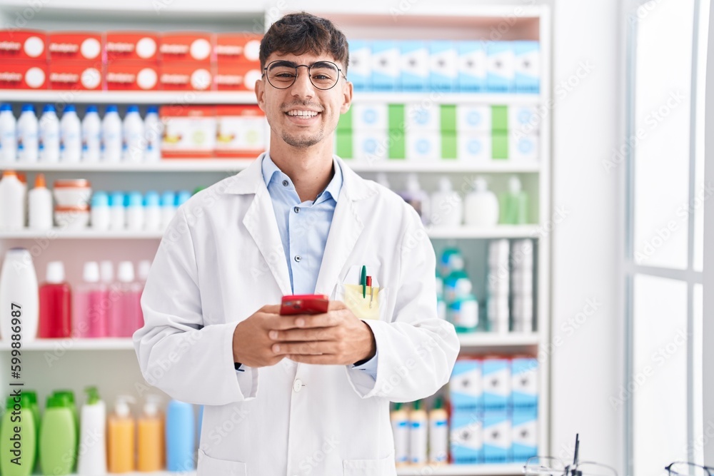 Young hispanic man pharmacist using smartphone working at pharmacy Young hispanic man pharmacist using smartphone working at pharmacy