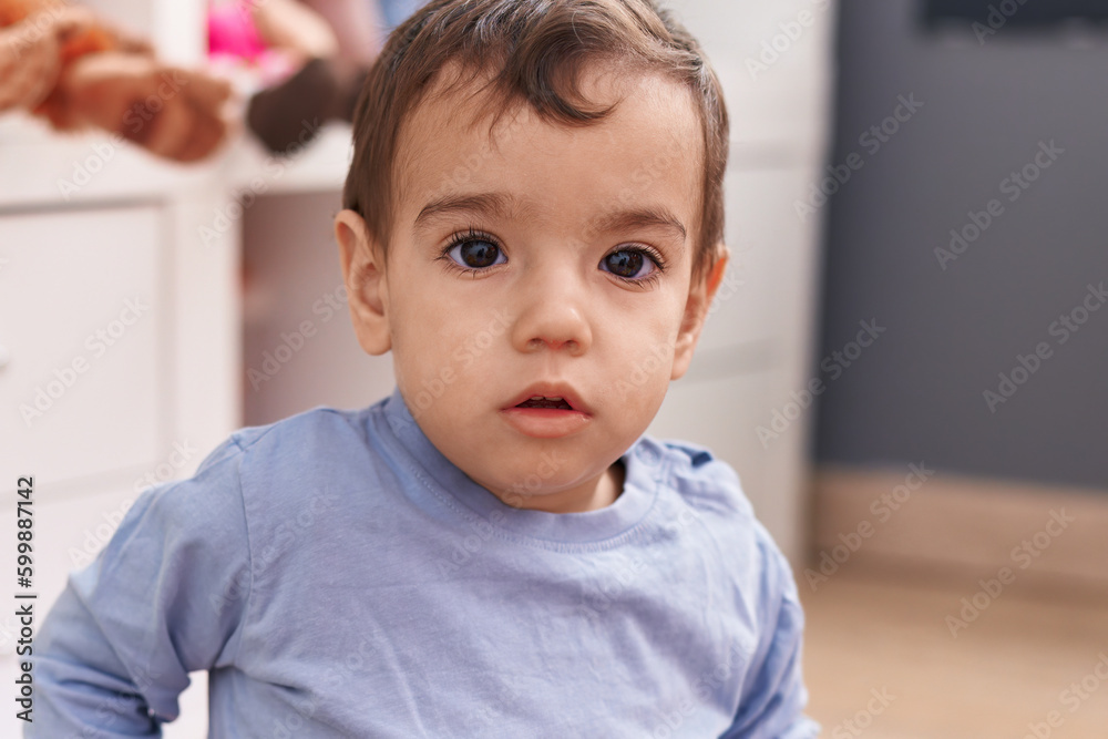 Adorable hispanic boy sitting on floor with relaxed expression at kindergarten