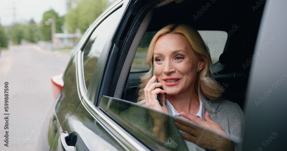 Beautiful adult caucasian woman rides on rear passenger seat of car, looking wonder out of the window during important phone call