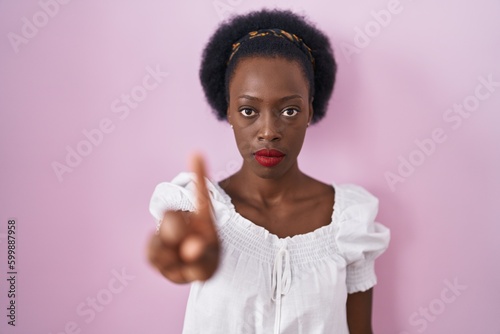 African woman with curly hair standing over pink background pointing with finger up and angry expression, showing no gesture