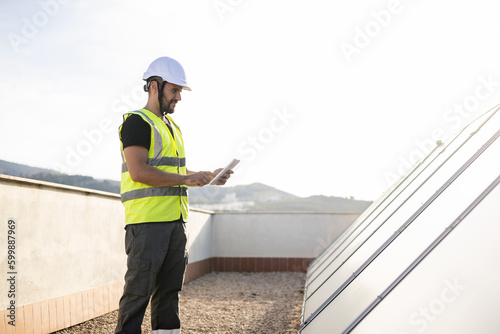 A specialized engineer in protective clothing is examining solar panels to heat the hot water in the houses using a digital tablet. Concept of solar panels, monitoring of solar panels. photo