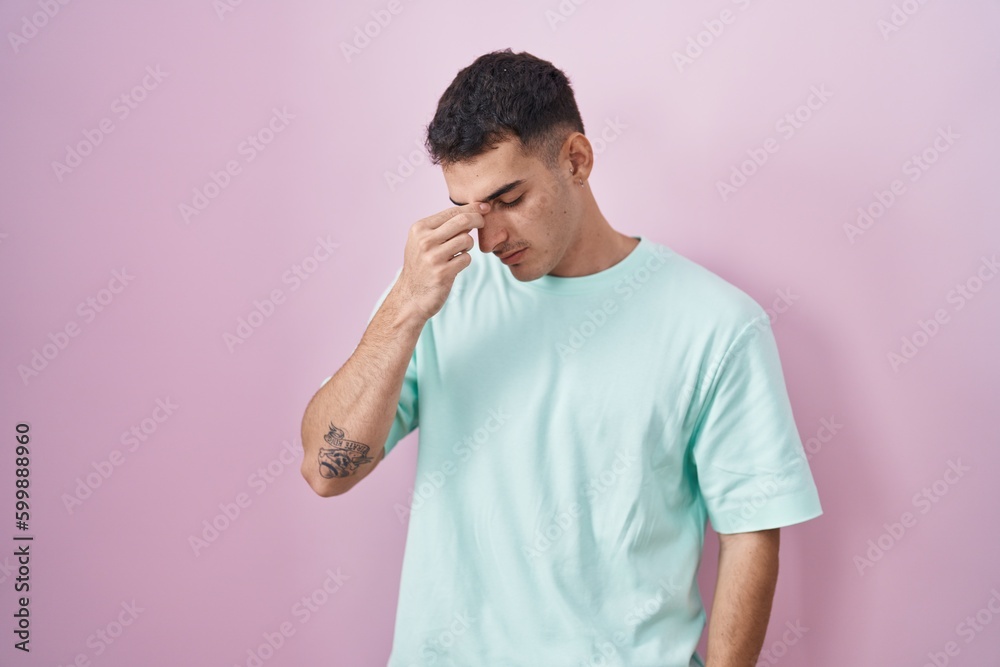 Handsome hispanic man standing over pink background tired rubbing nose and eyes feeling fatigue and headache. stress and frustration concept. Handsome hispanic man standing over pink background tired rubbing nose and eyes feeling fatigue and headache. stress and frustration concept.
