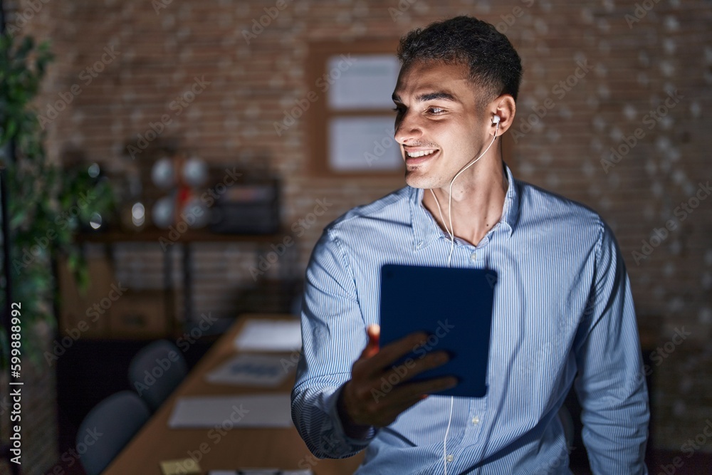 Handsome hispanic man working at the office at night looking away to side with smile on face, natural expression. laughing confident. Handsome hispanic man working at the office at night looking away to side with smile on face, natural expression. laughing confident.