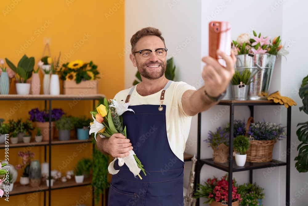 Middle age man florist make selfie by smartphone holding flowers at flower shop