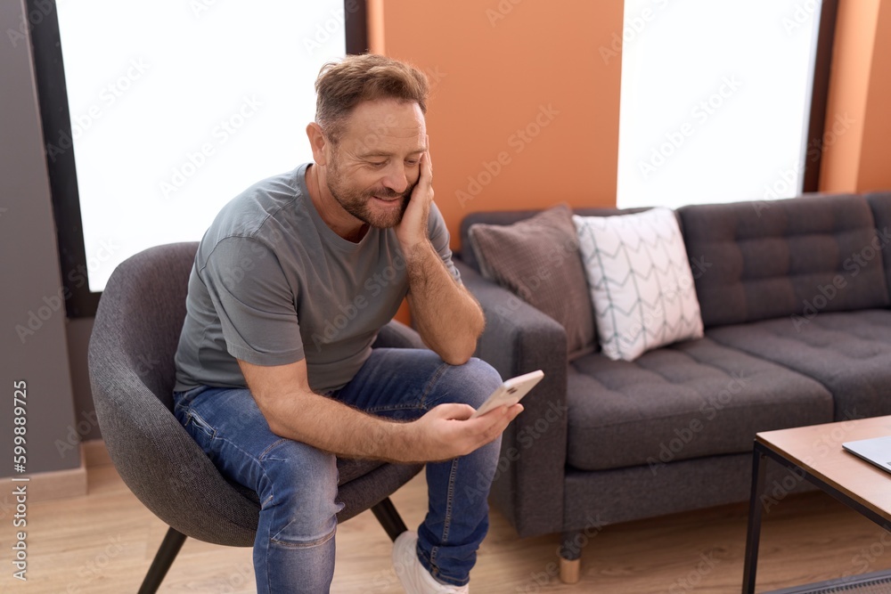 Middle age man using smartphone sitting on chair at home