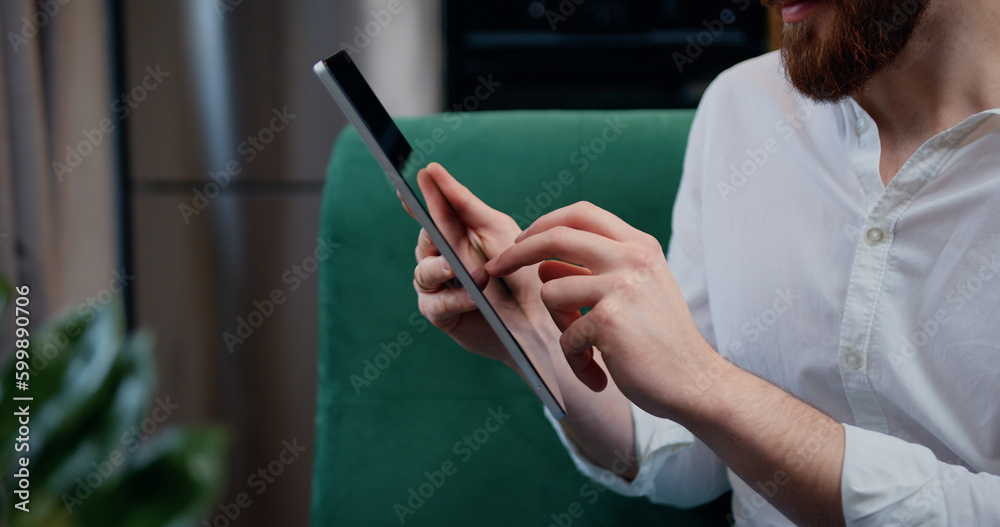 Man touching screen of digital tablet, hands of close-up. Businessman sitting on couch distance works for tablet online chatting with company investors.