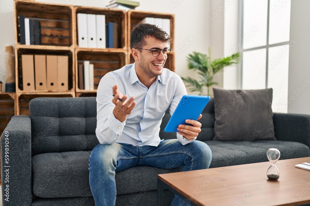 Young hispanic man psychologist smiling confident using touchpad at psychology clinic Young hispanic man psychologist smiling confident using touchpad at psychology clinic