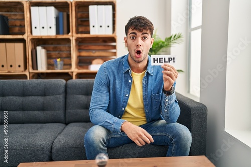 Young hispanic man at therapy asking for help scared and amazed with open mouth for surprise, disbelief face