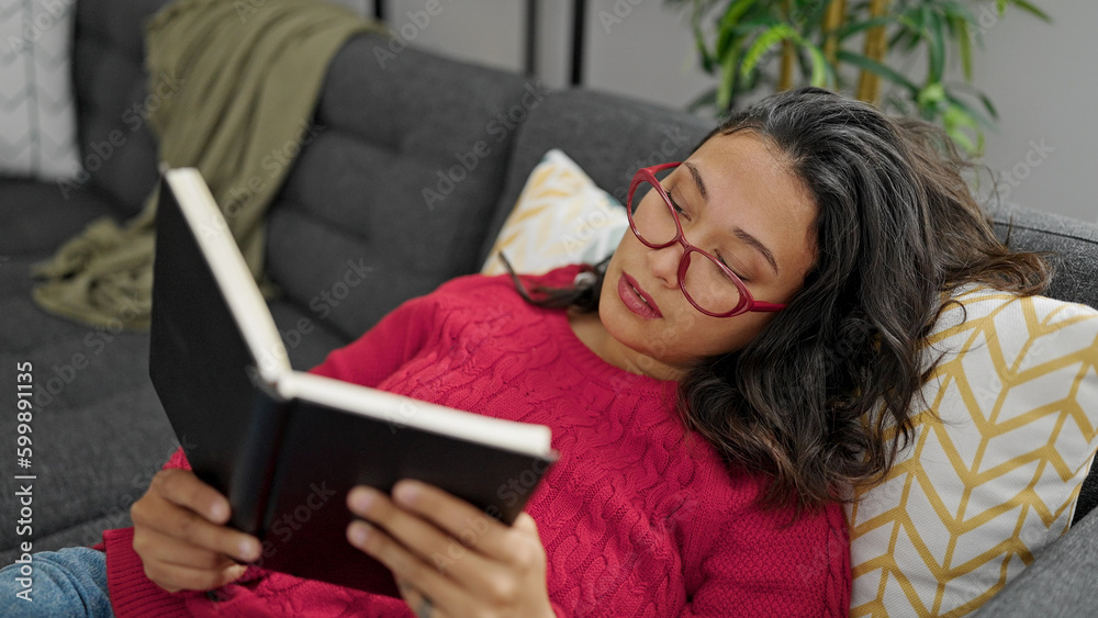 Young beautiful hispanic woman reading book lying on sofa at home Young beautiful hispanic woman reading book lying on sofa at home