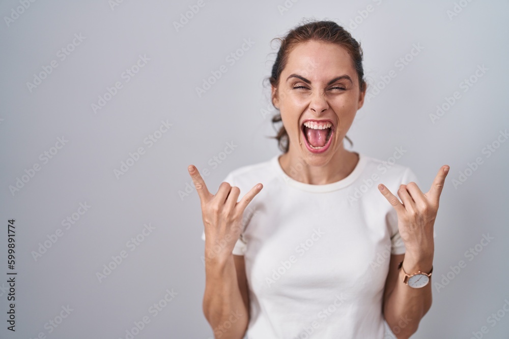 Beautiful brunette woman standing over isolated background shouting with crazy expression doing rock symbol with hands up. music star. heavy music concept. Beautiful brunette woman standing over isolated background shouting with crazy expression doing rock symbol with hands up. music star. heavy music concept.