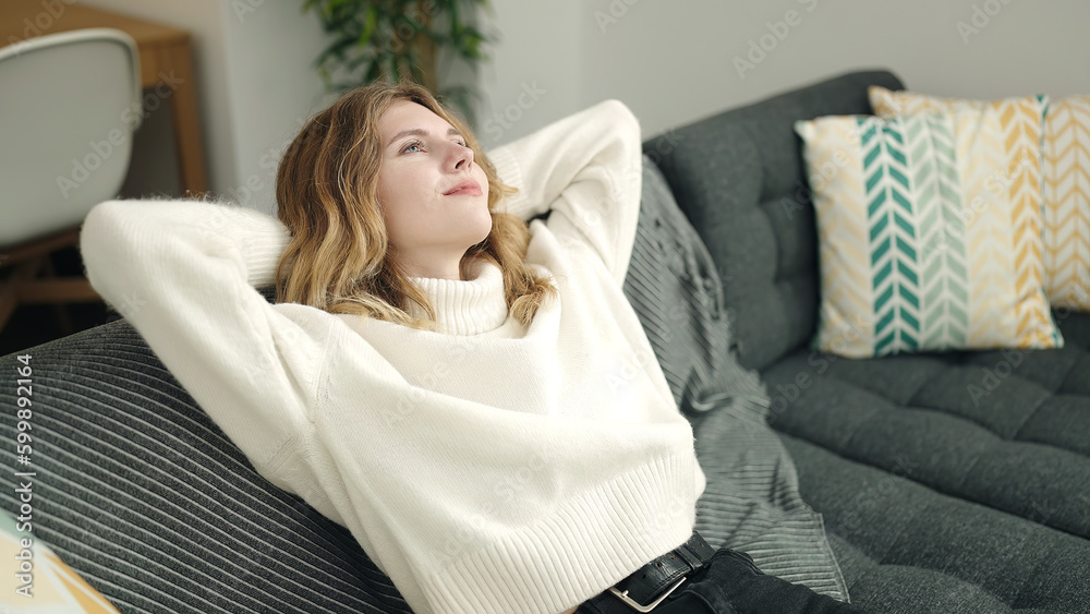 Young blonde woman relaxed with hands on head sitting on sofa at home Young blonde woman relaxed with hands on head sitting on sofa at home