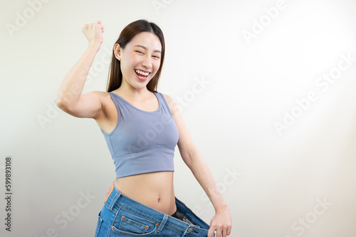 Asian woman wearing her old pant before loss weight feeling joyful with her body after diet success