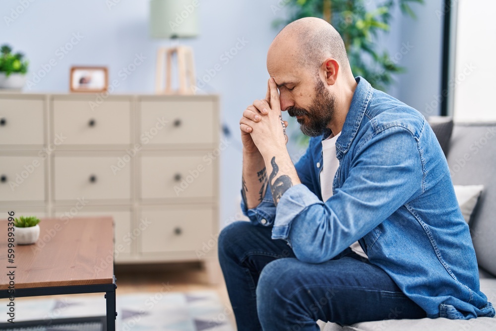 Young bald man stressed sitting on sofa at home Young bald man stressed sitting on sofa at home