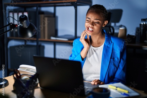 Beautiful african american woman working at the office at night touching mouth with hand with painful expression because of toothache or dental illness on teeth. dentist