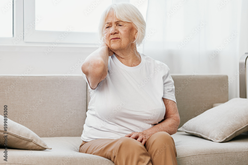 Elderly woman severe neck pain sitting on the sofa, health problems in old age, poor quality of life. Elderly woman severe neck pain sitting on the sofa, health problems in old age, poor quality of life.