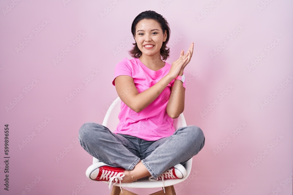 Hispanic young woman sitting on chair over pink background clapping and applauding happy and joyful, smiling proud hands together Hispanic young woman sitting on chair over pink background clapping and applauding happy and joyful, smiling proud hands together