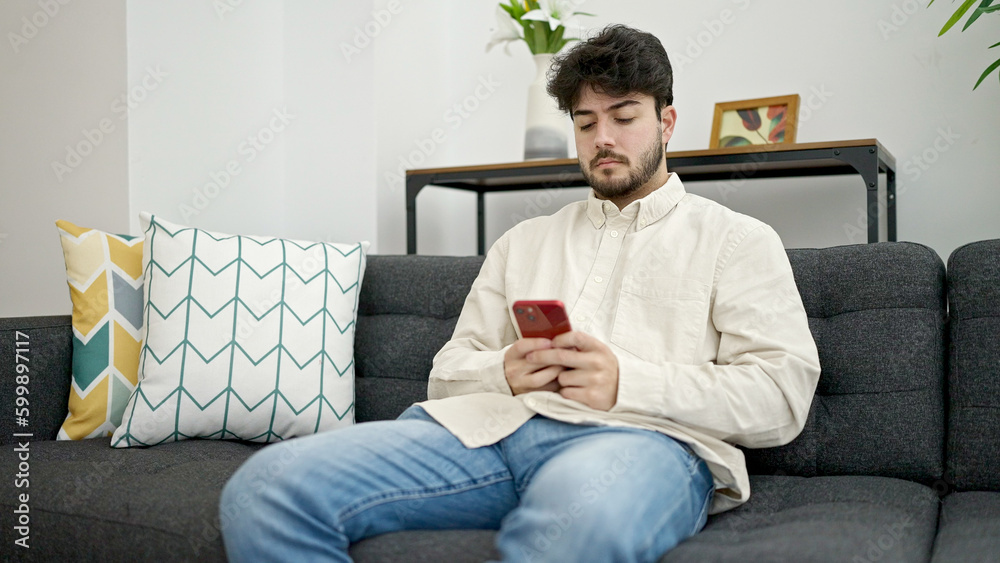 Young hispanic man using smartphone sitting on sofa at home Young hispanic man using smartphone sitting on sofa at home