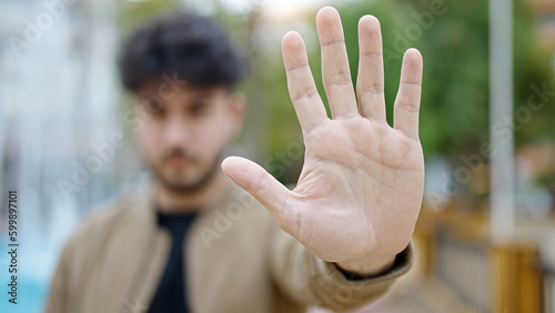 Young hispanic man doing stop gesture with hand at park
