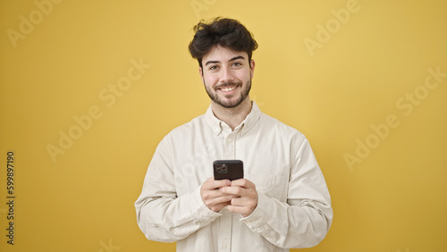 Young hispanic man using smartphone smiling over isolated yellow background