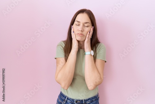 Beautiful brunette woman standing over pink background tired hands covering face, depression and sadness, upset and irritated for problem