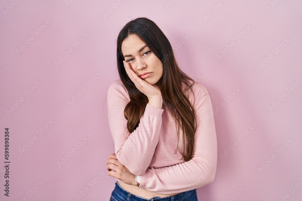 Young brunette woman standing over pink background thinking looking tired and bored with depression problems with crossed arms.