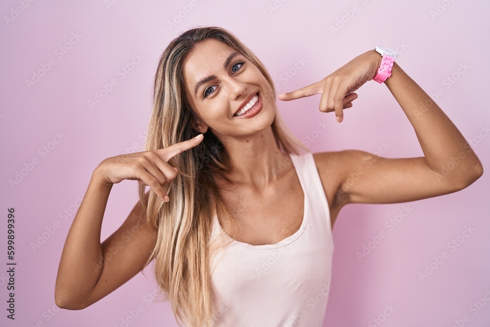 Young blonde woman standing over pink background smiling cheerful showing and pointing with fingers teeth and mouth. dental health concept. Young blonde woman standing over pink background smiling cheerful showing and pointing with fingers teeth and mouth. dental health concept.