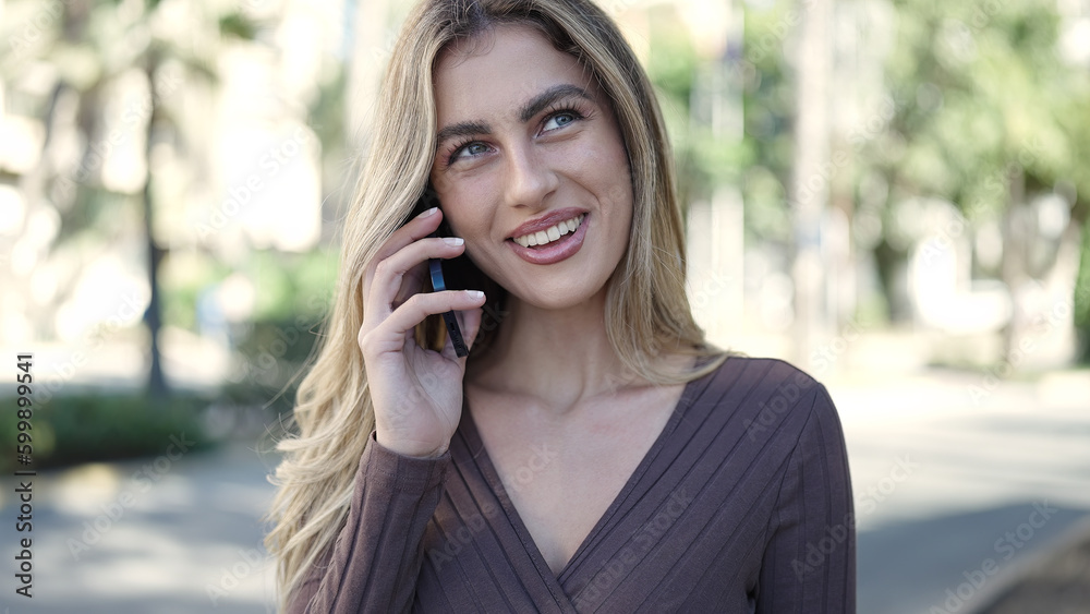 Young blonde woman smiling confident talking on the smartphone at park