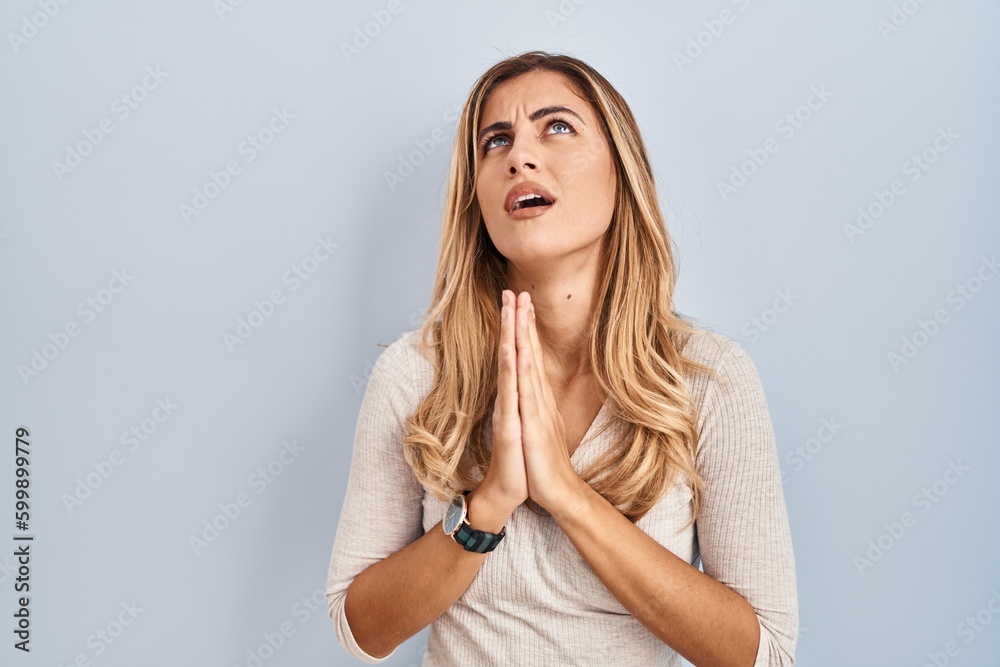 Fototapeta premium Young blonde woman standing over isolated background begging and praying with hands together with hope expression on face very emotional and worried. begging.