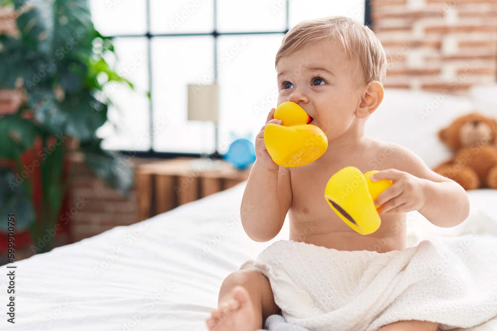 Adorable caucasian boy sucking duck toy sitting on bed at bedroom Adorable caucasian boy sucking duck toy sitting on bed at bedroom