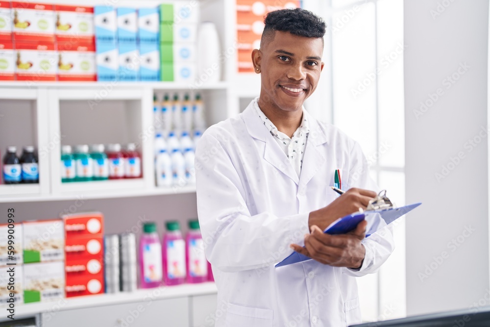 Young latin man pharmacist smiling confident writing report at pharmacy