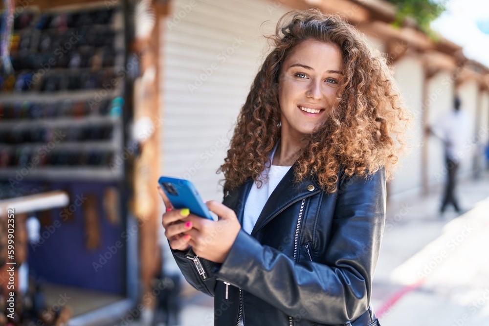Young beautiful hispanic woman smiling confident using smartphone at street market
