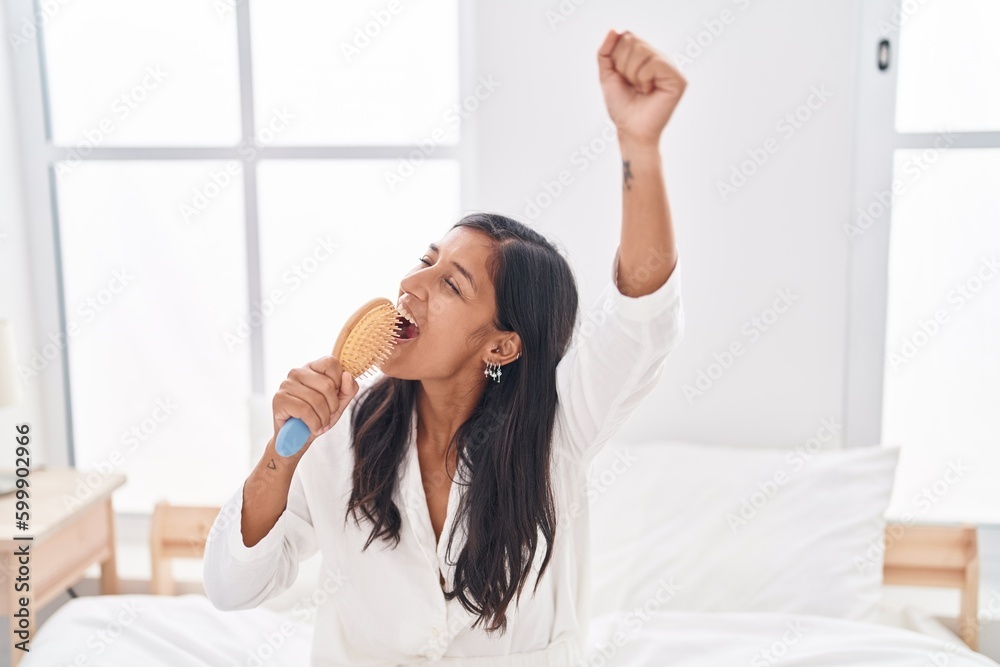 Young beautiful hispanic woman singing song using brush as a microphone at bedroom Young beautiful hispanic woman singing song using brush as a microphone at bedroom