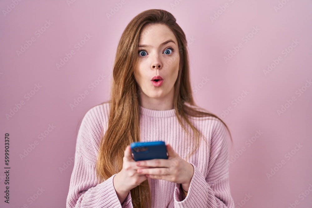 Young caucasian woman using smartphone typing message afraid and shocked with surprise and amazed expression, fear and excited face. Young caucasian woman using smartphone typing message afraid and shocked with surprise and amazed expression, fear and excited face.